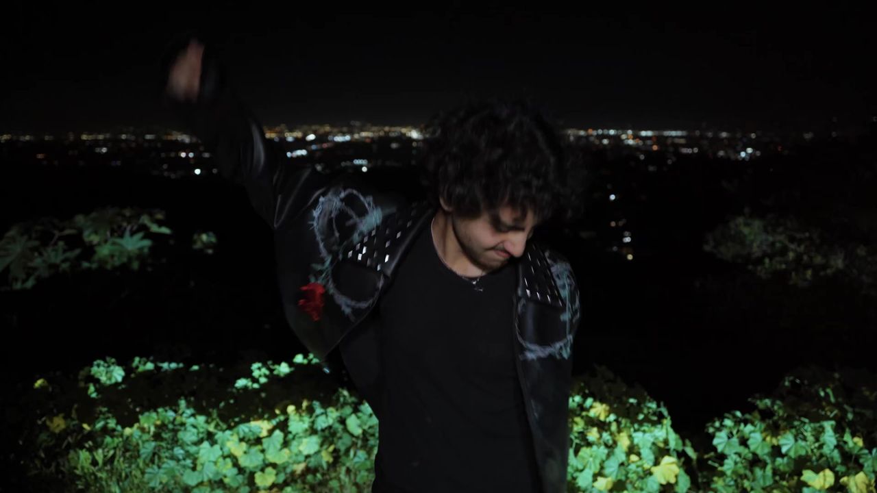 Still from the Demand music video: Lost in a black leather jacket above the city at night